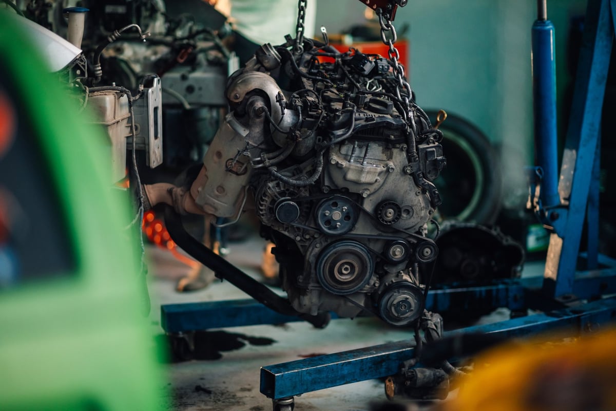 Close-up of an engine being detached from a car inside a garage during mechanical repair