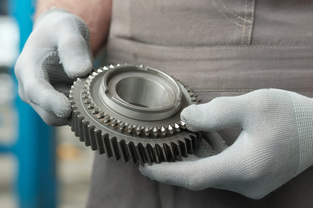 An auto mechanic holds a new gear in his hands for installation in the gearbox. Checking the part, its integrity, and preparing for replacement.