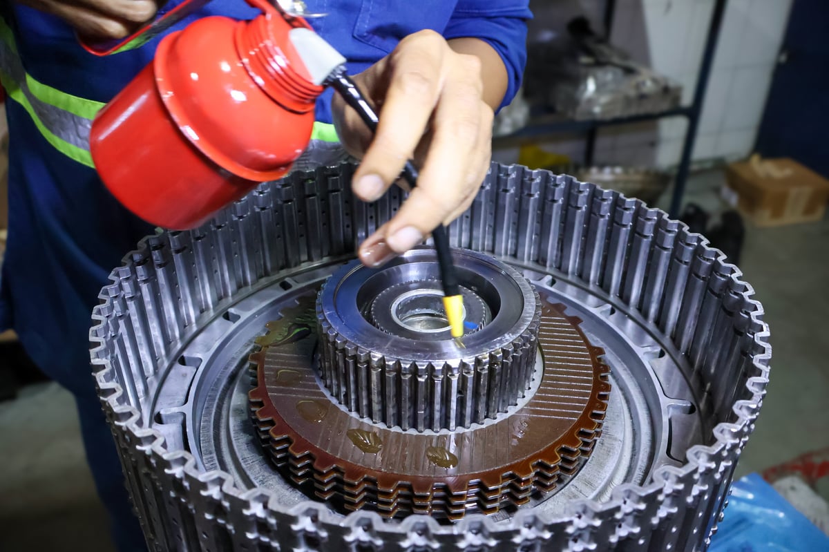 Close up of mechanic hands using a red oil pump can to lubricate friction discs and gear components during automatic transmission rotating clutch assembly